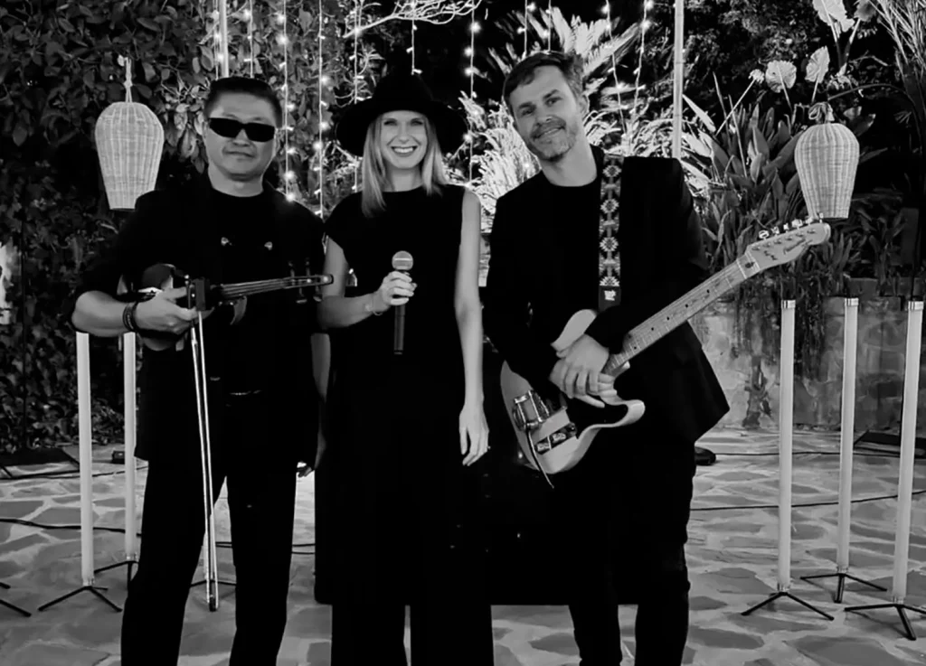 A trio of violin, vocals and guitar at an outdoor venue, in black and white
