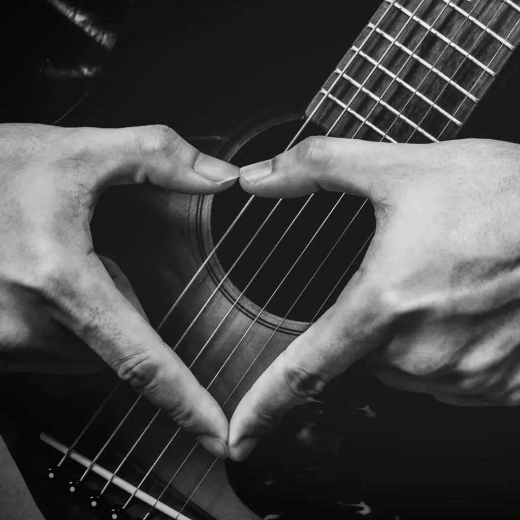 Two hands forming a heart over a guitar
